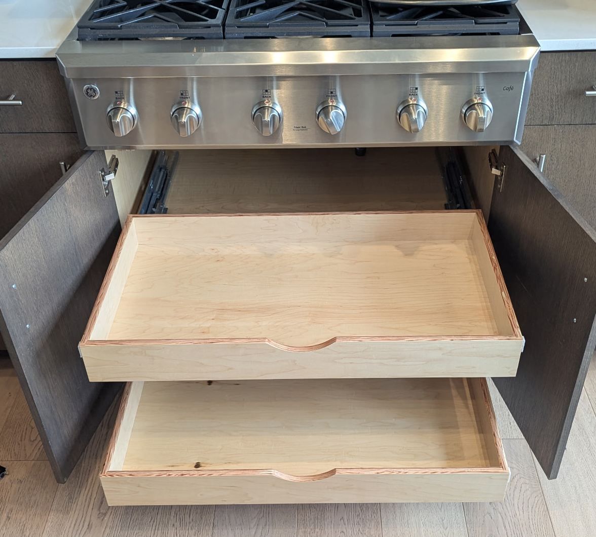Two pull-out shelves fully extended from the cabinet beneath a gas cooktop